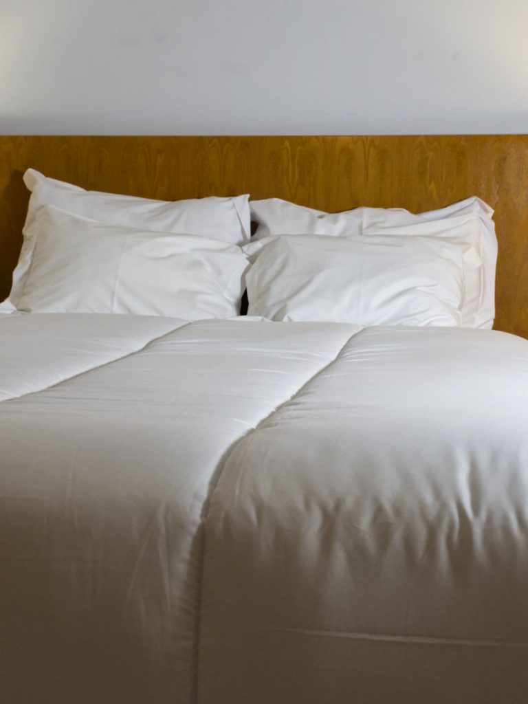 Cama feita com edredão nórdico branco de 400g e almofadas brancas, destacando um ambiente acolhedor.