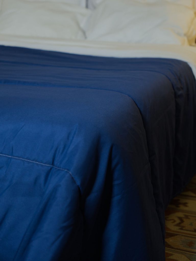 Detalhe do edredão nórdico azul 200g sobre a cama, evidenciando a textura e queda natural do tecido.