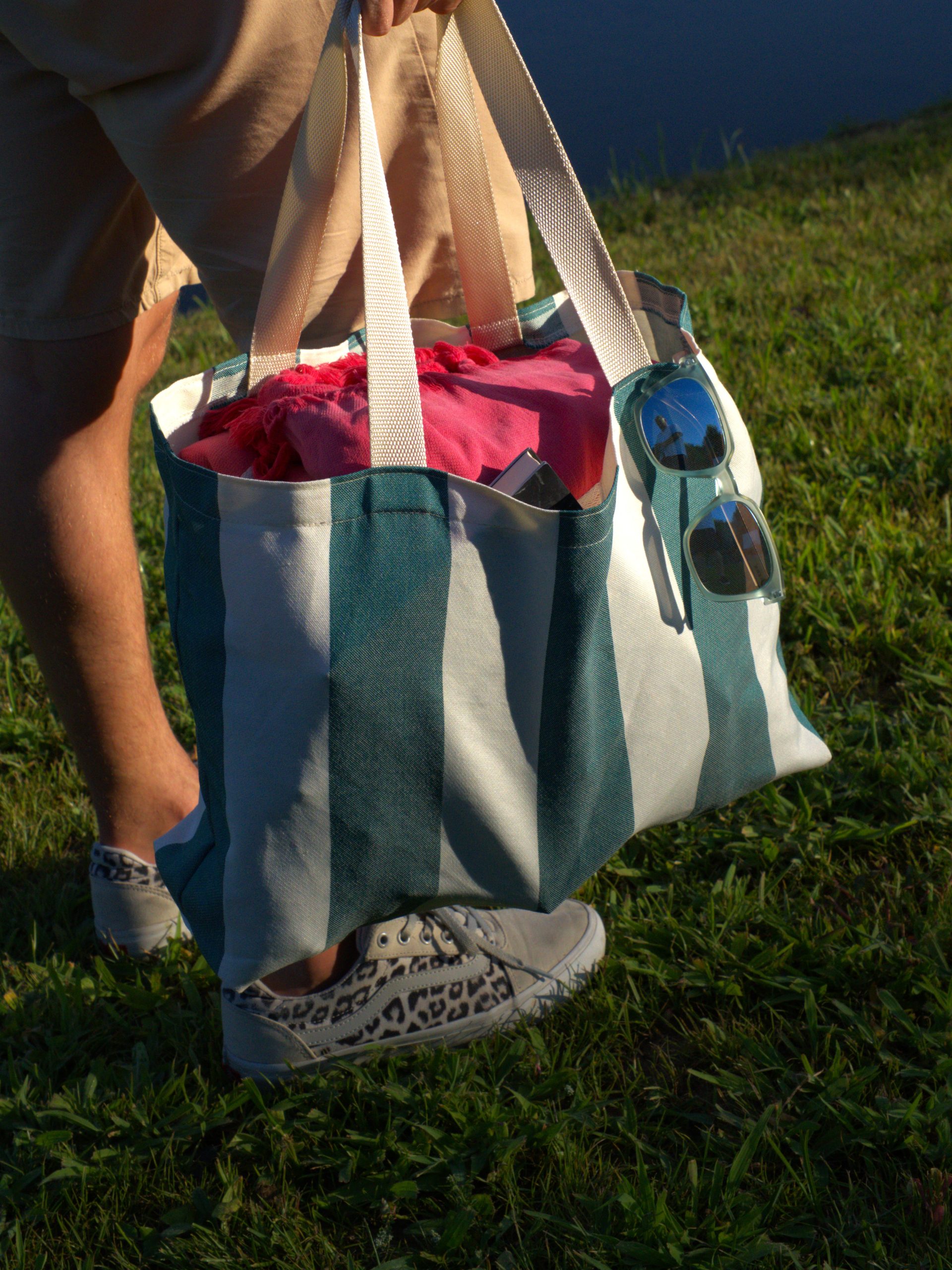 Saco de praia com riscas verticais verdes e brancas em tecido de poliéster, LeCamaleon, captado em ambiente natural com relva – ideal para verão, compras e uso diário.